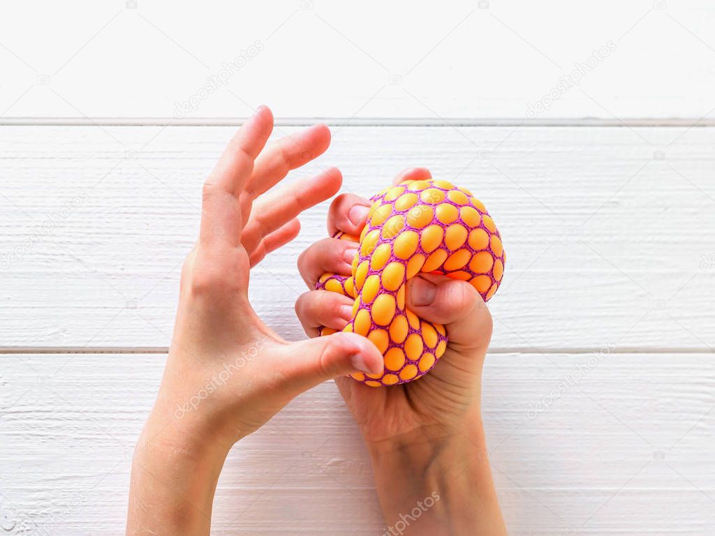 Toy against stress in the hands of a child on a white wooden table.