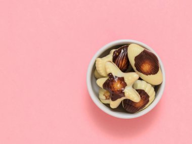 Beyaz kâse, pembe arka planda deniz kabuğu şeklinde tatlılar. Düz yatıyordu.