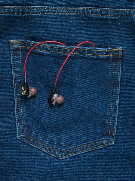 Rot mit schwarzen Kopfhörern, die aus der Tasche einer blauen Jeans herausragen. — Stockfoto