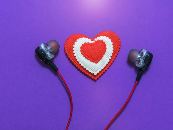 Coração de cores brancas e vermelhas em fones de ouvido em fundo roxo. Depósito plano . — Fotografia de Stock