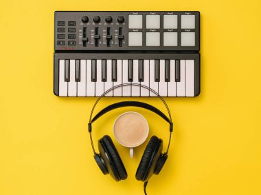 Kulaklıklar, kahve Fincanı ve sarı arka planda müzik mikseri. İşyeri organizasyonu kavramı.