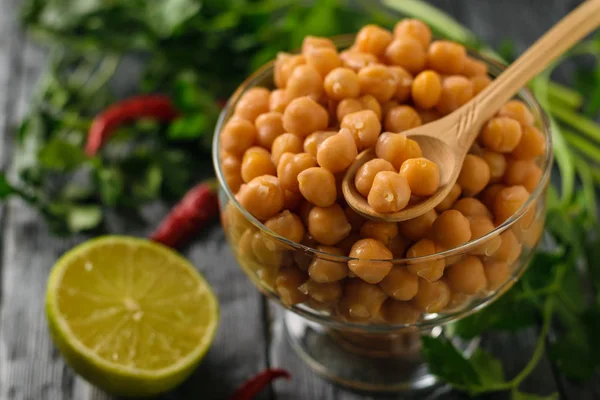 Pois chiches bouillis dans un bol en verre, poivre et citron vert sur une table . — Photo