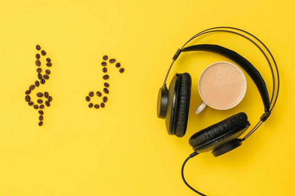 Note di chicchi di caffè, cuffie e una tazza di caffè su sfondo giallo. Il concetto di scrivere musica. La vista dall'alto . — Foto Stock