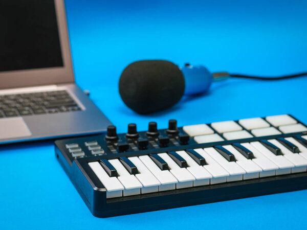 Music mixer, open laptop and microphone with wires on blue background. Equipment for recording music tracks.