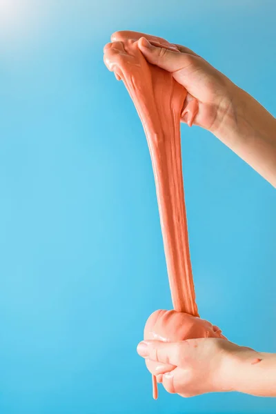 Orange slime stretch two hands on a turquoise background.