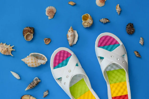 Kolorowe buty i dużo muszli morskich na niebieskim tle. Koncepcja wakacji nad morzem. Płaski lay. — Zdjęcie stockowe