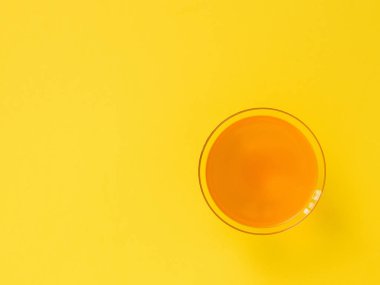 Parlak sarı arka planda cam turuncu içecek. Minimalizm. Düz yatma.