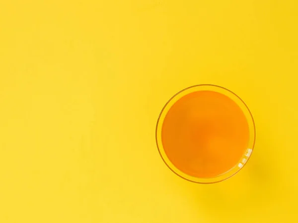 Bebida naranja en vaso sobre fondo amarillo brillante. Minimalismo. Puesta plana . — Foto de Stock