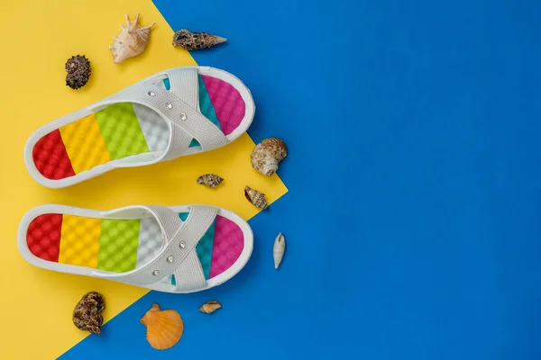 Zapatos coloridos y un montón de conchas marinas sobre un fondo azul y amarillo. El concepto de unas vacaciones junto al mar. Puesta plana . — Foto de Stock
