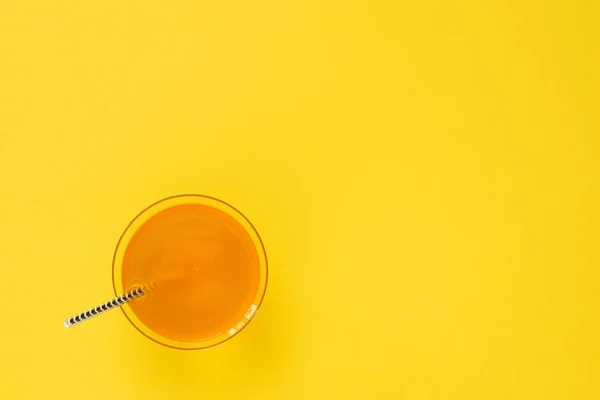 Vaso con bebida naranja y paja de cóctel sobre fondo amarillo. Minimalismo. Puesta plana . — Foto de Stock