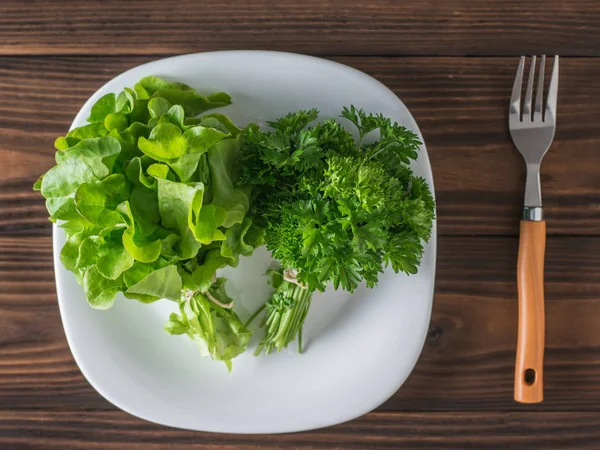 Alface e salsa em uma tigela branca em uma mesa de madeira com um garfo. Depósito plano . — Fotografia de Stock