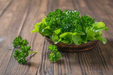 Tahta bir masa üzerinde kil bir kapta marul ve maydanoz.