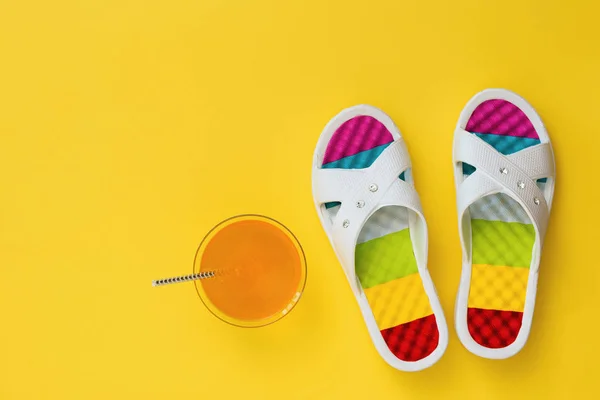 Bebida naranja y pizarras con suelas de colores sobre fondo amarillo. El concepto de vacaciones de verano. Puesta plana . — Foto de Stock