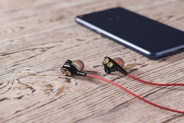 Headphones with red cord and a blue tinted smartphone on a wooden table. Sports style.