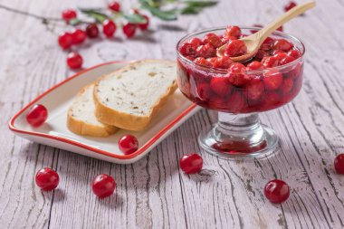 Ahşap bir masada bir kase kiraz reçeli ve kaba un ekmeği.