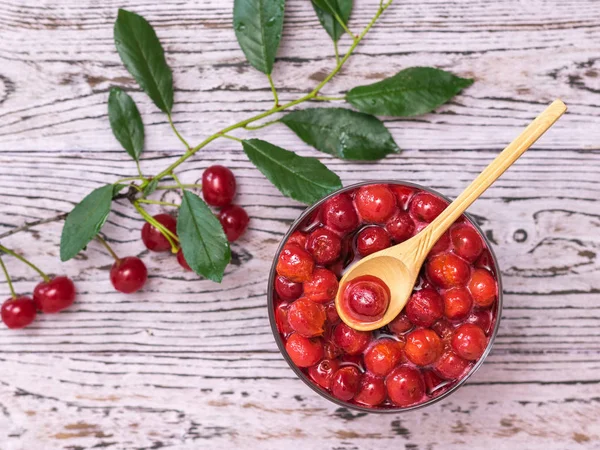 A sprig of cherry berries and a bowl of cherry jam on a wooden table. Homemade jam from the fresh harvest of cherry berries. Flat lay.