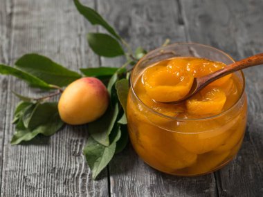 Bir kavanoz kayısı reçeli ve masada bir kavanoz yeşil yaprak.