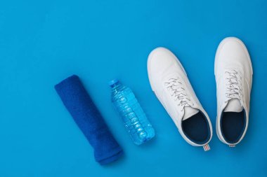 Mavi havlu, beyaz spor ayakkabılar ve mavi arka plan üzerine su şişesi. Spor tarzı. Düz yatıyordu.