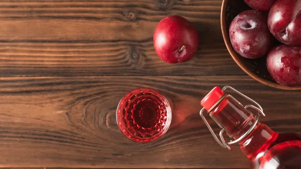 Сливовый алкогольный напиток и сливовые ягоды на коричневом столе. Плоский лежал . — стоковое фото