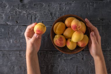 Tahta bir masada bir kase de taze kayısı tutan çocukların elleri.