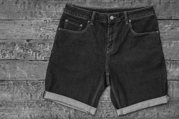 Zwart-wit foto van denim shorts op houten achtergrond. Modieuze Unisex kleding. — Stockfoto