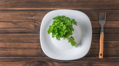 Maydanoz bir demet büyük bir ahşap masada bir çatal ile beyaz bir tabak üzerinde bırakır. Düz yatıyordu.