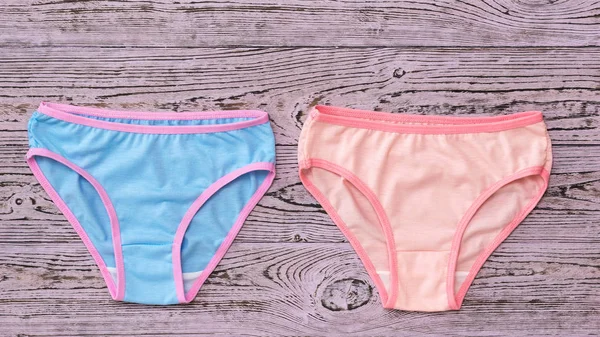 Lying next to pink and blue women's panties on a wooden background. Fashionable concept. Beautiful lingerie. The view from the top. — Stock Photo, Image