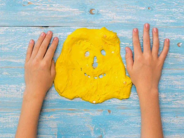 Les mains de l'enfant sur la table à côté du visage d'une boue jaune . — Photo