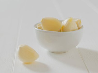 Beyaz bir masada soyulmuş sarımsak ile porselen kase. Geleneksel tıbbın bileşeni.