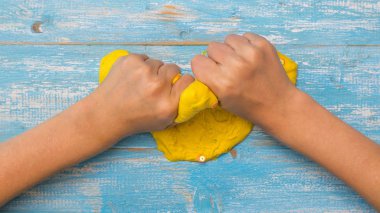 Çocuğun elleri ahşap bir masaüzerinde parlak sarı balçık buruşturuyor.