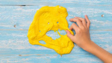 Sarı balçıktan yapılmış komik bir yüz ve mavi bir masada bir çocuğun eli..