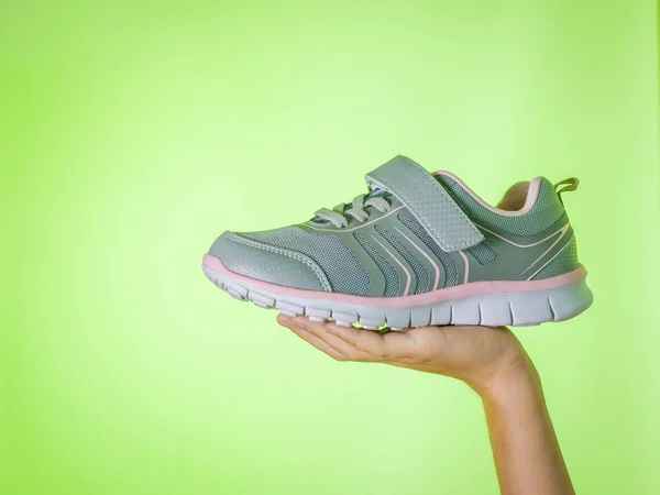 Fashionabla grå sneakers i ett barns hand på en grön bakgrund. Färg trend. — Stockfoto