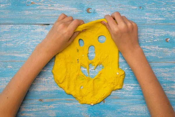 The girl stretches a face of yellow slime on a wooden table.