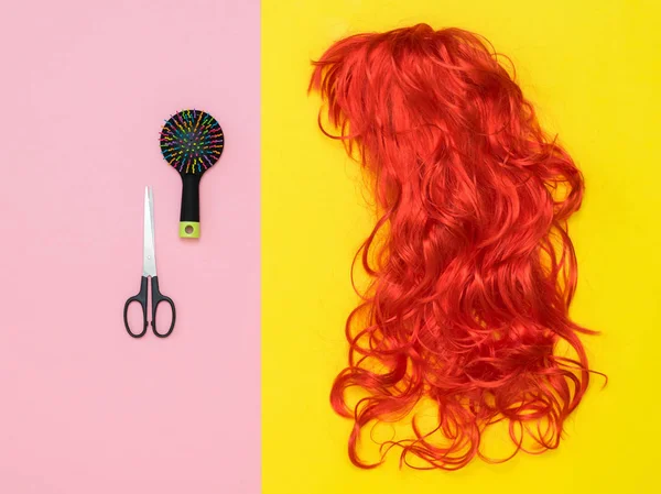 Forbici, pettine e parrucca arancione su sfondo giallo e rosa. Accessori per creare stile. Posa piatta . — Foto Stock