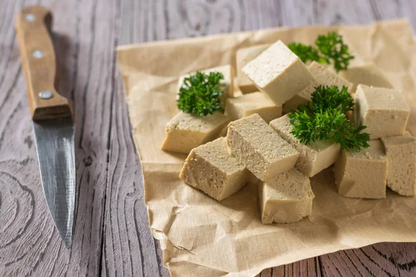 Des morceaux de tofu frais sur du papier avec un couteau sur la table. Fromage de soja . — Photo