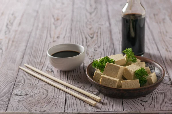 Uma garrafa de molho de soja e fatias de queijo tofu em uma mesa de madeira. Queijo de soja . — Fotografia de Stock