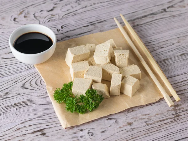 Wooden sticks with slices of tofu cheese and soy sauce on a wooden table. Soy cheese. — Stock Photo, Image