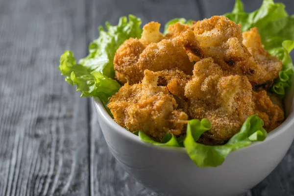 A deep bowl of lettuce and sauteed cauliflower on a wooden table. — Stock Photo, Image