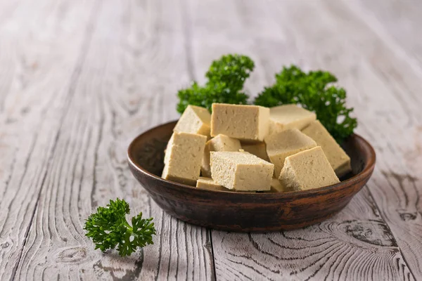 Une plaque d'argile avec du tofu et des feuilles de persil bouclés sur une table en bois . — Photo