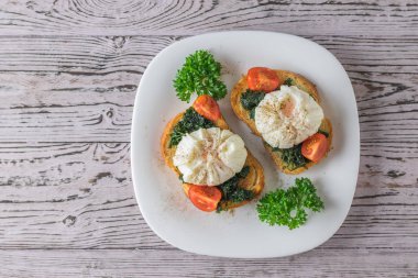 Kızarmış ekmeğin üzerinde haşlanmış yumurta ve beyaz tabakta otlar. Yukarıdan görünüşü.