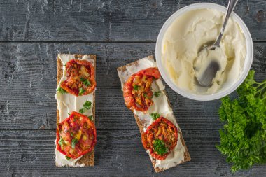 Bir kavanoz krem peynir ve ahşap bir masada güneşte kurutulmuş domatesli tost. Düz yatıyordu.