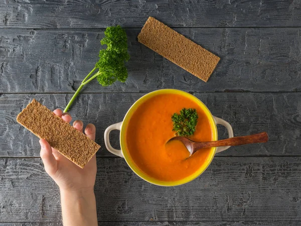 Cream of pepper soup and a child's hand with toast on a wooden table. Flat lay. — Stock Photo, Image