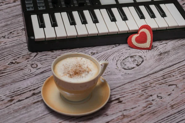Una taza de café capuchino con canela y una batidora de música en una mesa de madera . — Foto de Stock