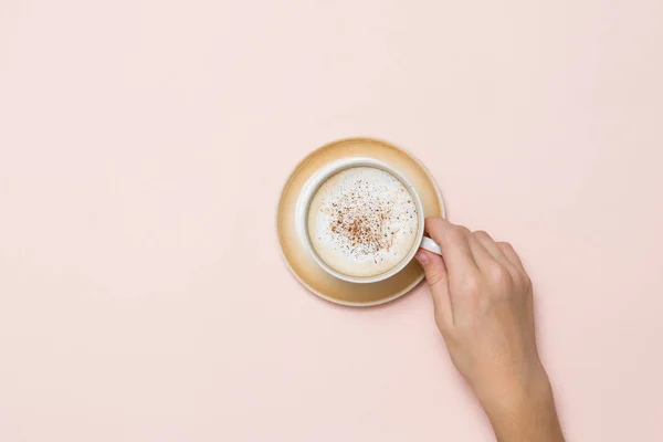Mercan zemininde kremalı ve tarçınlı bir fincan kahveyi tutarken.