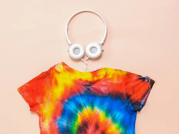 A bright tie dye t-shirt with headphones on a pastel background. Flat lay. Pastel color. — Stock Photo, Image