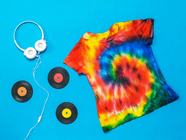 Witte koptelefoon, vinyl schijven en een stropdas kleurstof t-shirt op een blauwe achtergrond. Plat gelegd. Pastelkleur. — Stockfoto