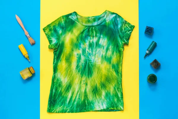 T-shirt amarela e verde em estilo tie dye e pintura sobre um fundo azul e amarelo. Depósito plano . — Fotografia de Stock