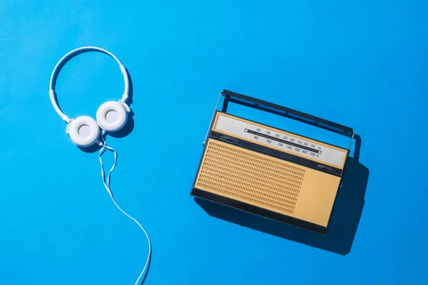 Rádio retrô e fones de ouvido brancos em um fundo azul em luz dura. Técnica vintage . — Fotografia de Stock