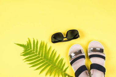 Sarı arka planda güneş gözlüğü, palmiye yaprağı ve sandaletler..
