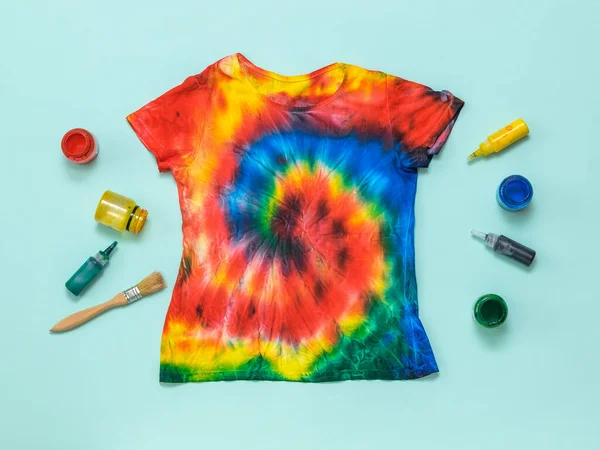 T-shirt pintada à mão em estilo tie dye e pintura sobre um fundo azul claro. Depósito plano . — Fotografia de Stock